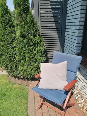 Une chaise en bois avec un coussin et un revêtement bleu, placée sur une terrasse en briques.