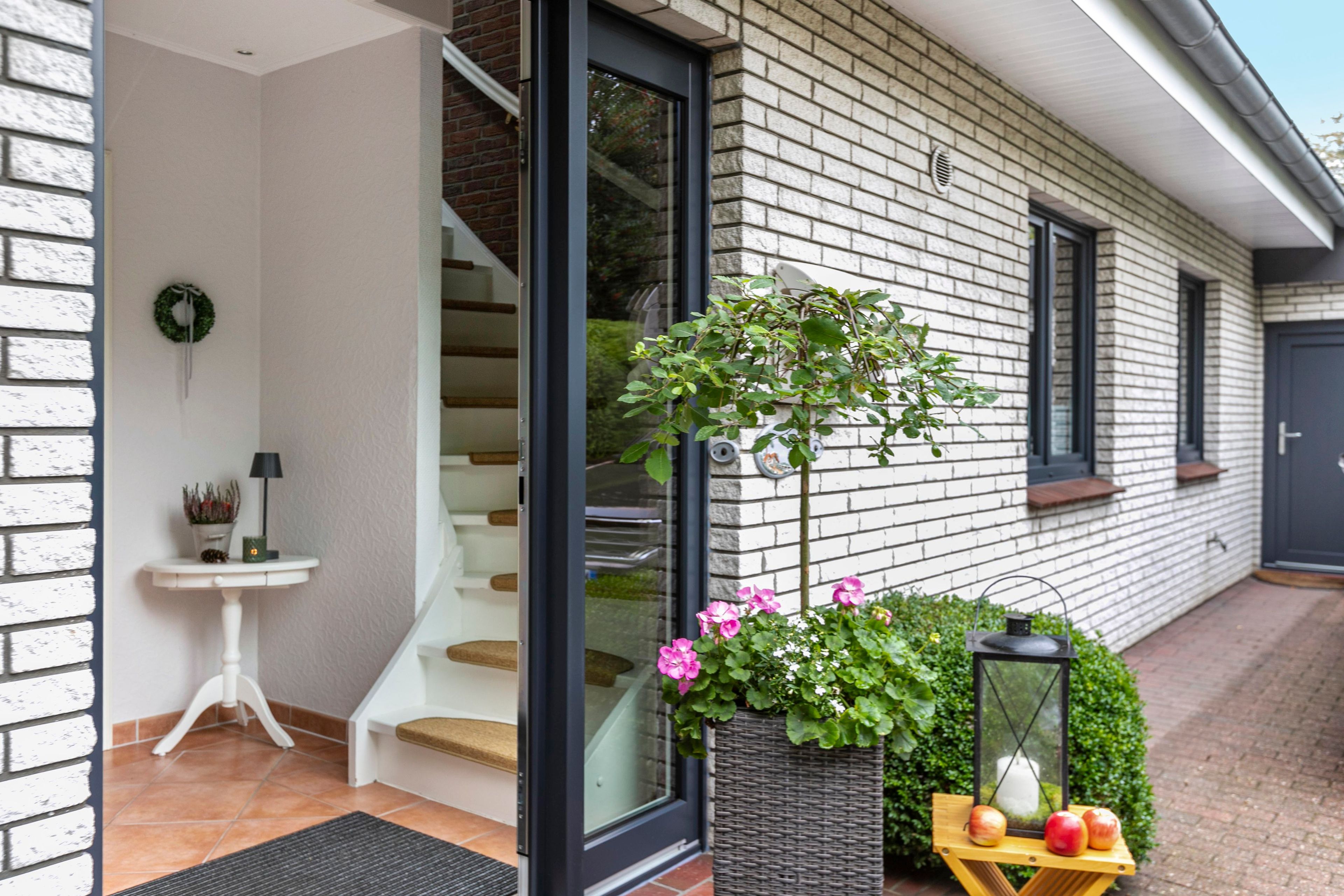 Een modern huis met een trap, een kleine tafel met een lamp en een bloemenplanter.