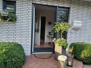 A brick exterior with a door leading to an interior space, a small outdoor seating area with a table and chairs, and a potted plant with flowers. - Apartment 'Ferienwohnung Schwalbennest' with Wi-Fi (Niebüll)