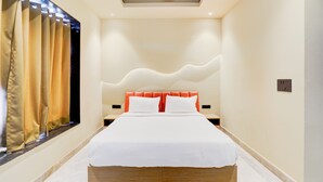 A hotel room with a large bed, a headboard with a wavy design, and a window with curtains. - Hotel Royal City (Noida)