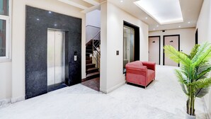 A modern interior with a staircase, a red armchair, and a potted plant. - Hotel Royal City (Noida)