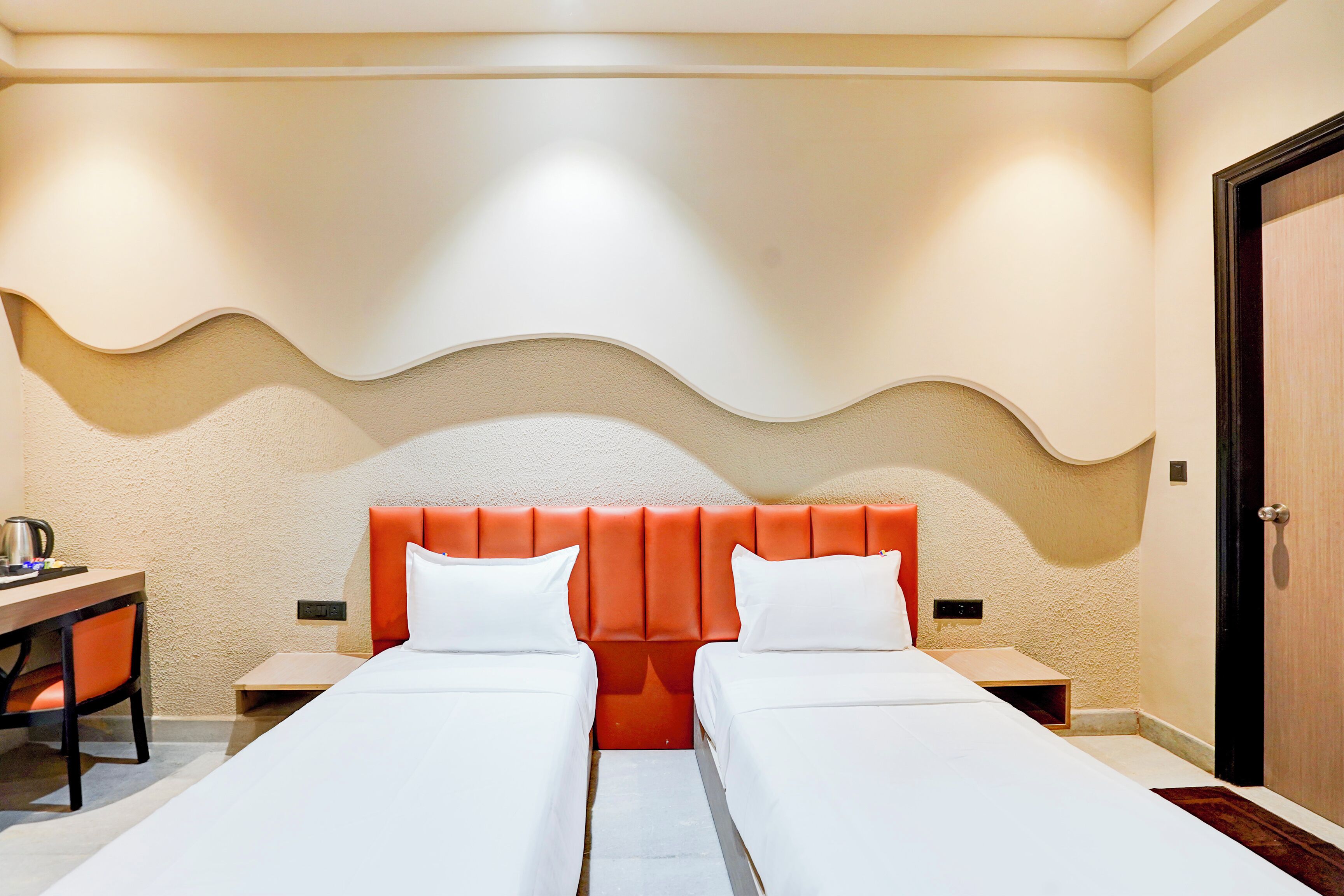 A hotel room with two single beds, a desk, and a chair.