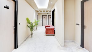 A hallway with a marble floor, a red sofa, and potted plants. - Hotel Royal City (Noida)