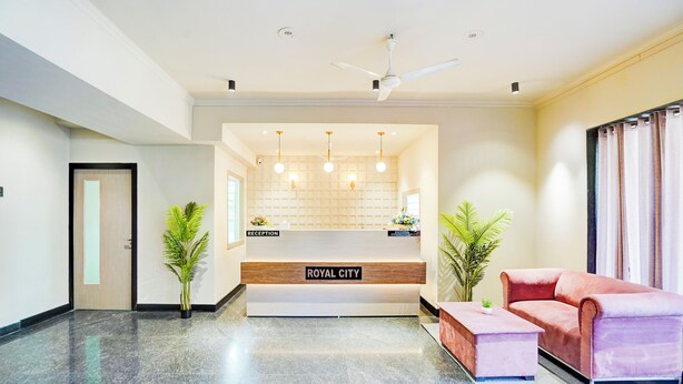 A reception area with a reception desk labeled "ROYAL CITY," a ceiling fan, pendant lights, and a pink sofa. - Hotel Royal City (Noida)