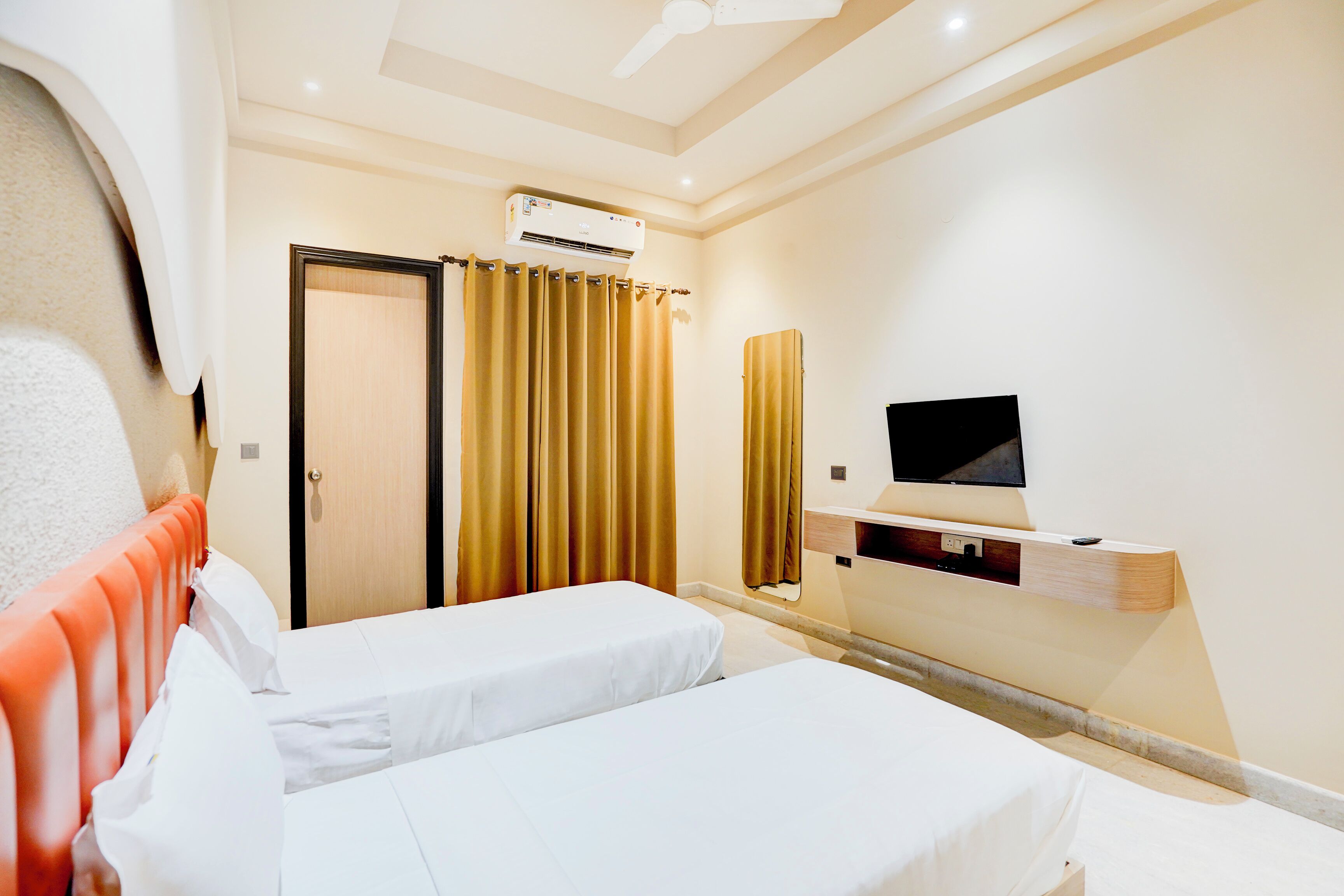Habitación de hotel con dos camas, televisión, aire acondicionado y una puerta con cortinas.