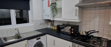 A compact kitchen with a washing machine, a stove, and a microwave.
