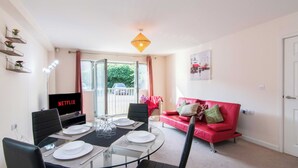 A dining area with a glass table, chairs, and a TV displaying 'NETFLIX'. - Coventry 2-bedroom Apartment-pet Friendly (Coventry)