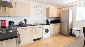 A modern kitchen with light wood cabinets, a stainless steel refrigerator, a built-in washing machine, and a wall clock. - Coventry 2-bedroom Apartment-pet Friendly (Coventry)