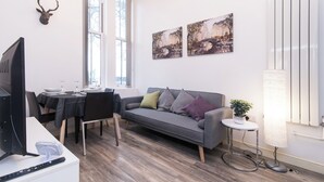 A modern living room with a grey sofa, a dining table with chairs, a mounted deer head, and two landscape paintings on the wall. - Tranquil Derby 2 Bedroom Apartment Retreat (Derby)