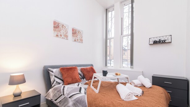 A modern bedroom with a bed, bedside table, lamp, and artwork on the wall. - Tranquil Derby 2 Bedroom Apartment Retreat (Derby)