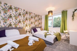 A hotel room with two beds, green curtains, a window with a view, and a plant on the window sill. - Michaelmas 2-bedroom Apartment in Coventry (Coventry)