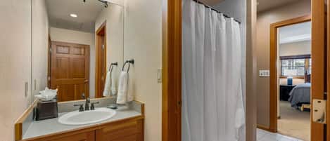 A bathroom with a wooden vanity, a large mirror, a white sink, and a shower curtain.
