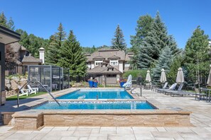 A swimming pool with lounge chairs and umbrellas, surrounded by trees and a building in the background. - Spectacular views | Private Hot Tub | Sleeps 16 (Beaver Creek)