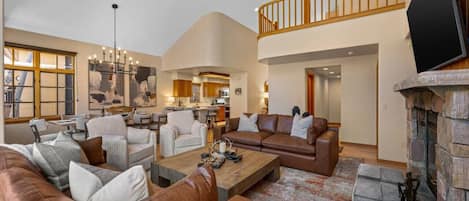 A spacious living room with a high ceiling, a fireplace, and a dining area visible in the background.