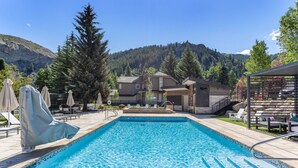 Una piscina con acqua cristallina, circondata da lettini e ombrelloni, con le montagne sullo sfondo.