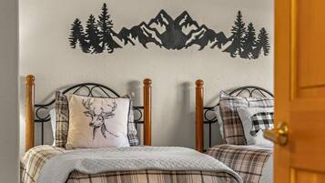 Un dormitorio con dos camas, cada una con cabecera, un adhesivo mural con motivos de montaña y una puerta a la derecha.