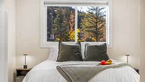 A bedroom with a large window, a bed with white bedding, two pillows, a blanket, and a nightstand with a lamp. - New | Prime Location | Skier`s Paradise (Avon)