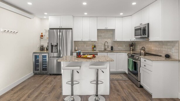 A modern kitchen with white cabinets, stainless steel appliances, a granite countertop, and two bar stools. - New | Prime Location | Skier`s Paradise (Avon)