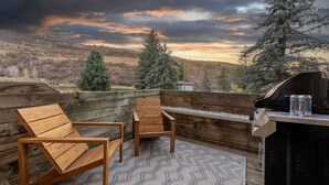 An outdoor patio with two wooden chairs, a grill, and a view of a forested landscape. - New | Prime Location | Skier`s Paradise (Avon)