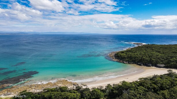 Paisagem costeira com praia, águas turquesa cristalinas e área arborizada.
