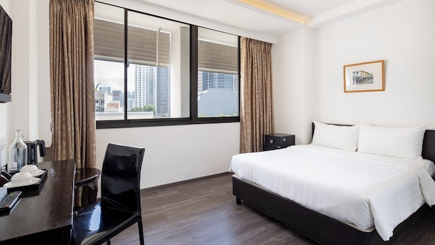Une chambre d’hôtel avec un lit, un bureau et une chaise, une télévision et une fenêtre avec des rideaux.