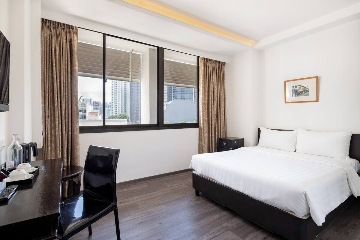 A hotel room with a bed, a desk with a chair, a TV, and a window with curtains.