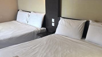 A hotel room with two beds, each with white linens and pillows. There are framed pictures on the walls, one of a plant and another of a landscape.