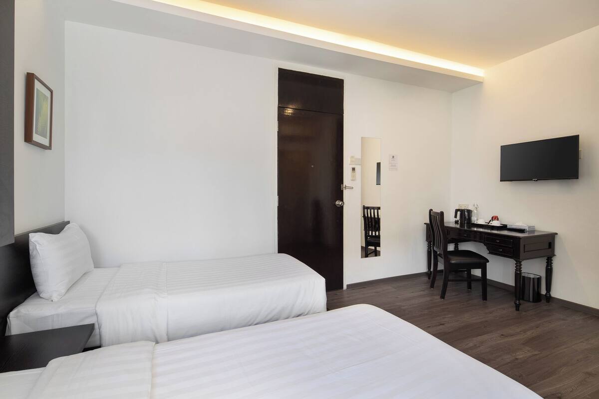 A hotel room with two beds, a desk, a chair, a television, and a door.