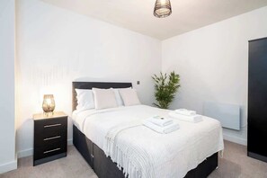 A bedroom with a bed, bedside table, lamp, and a potted plant. - City Escape: Chic 1 Bed Apt in Central Leeds (Leeds)