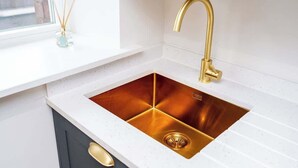 Una cocina con encimera blanca, pileta dorada y grifo dorado.