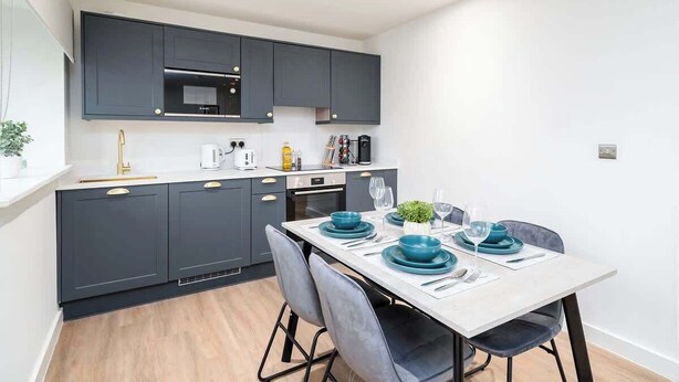 Una cocina moderna con armarios oscuros, una encimera blanca y una mesa de comedor dispuesta con platos y vasos azules.