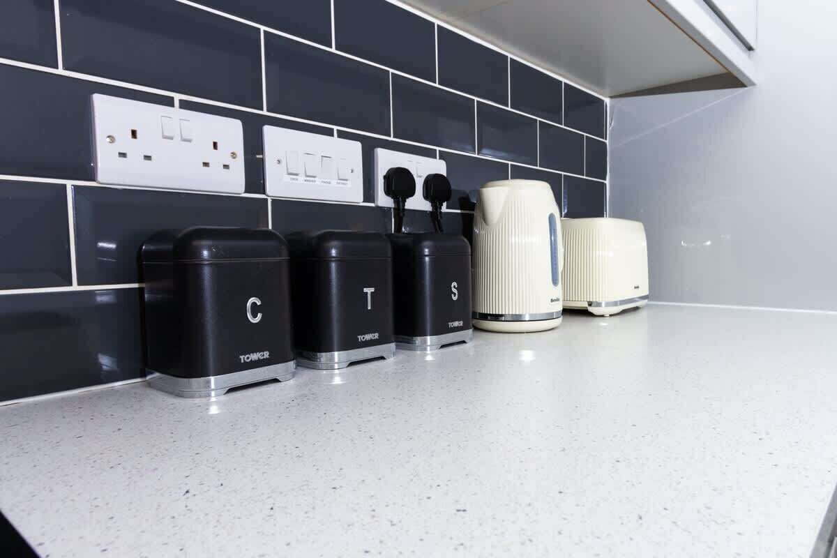 Una cocina con tres electrodomésticos negros etiquetados C, T y S, y un electrodoméstico blanco sobre la encimera.