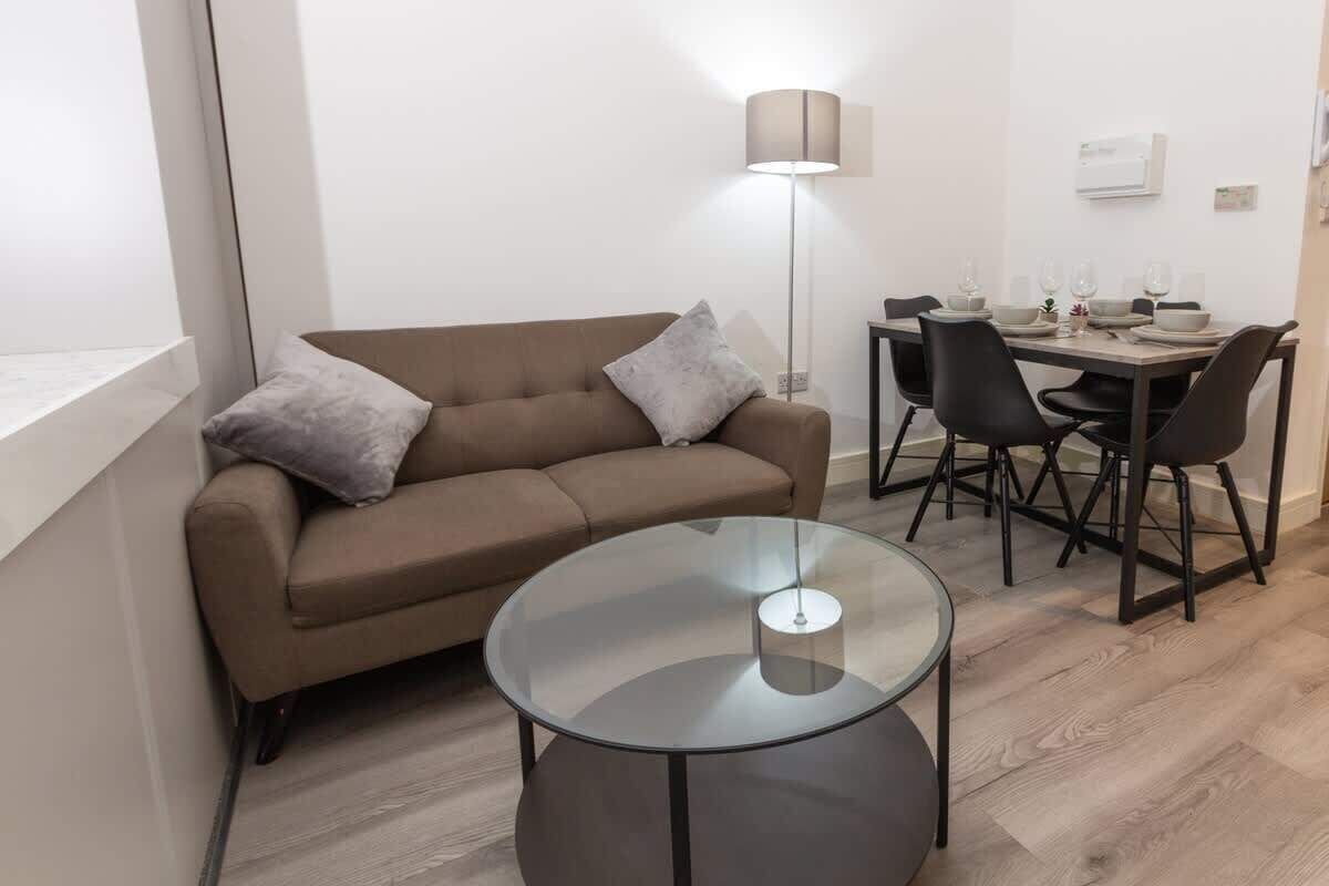 A modern living room with a sofa, a glass coffee table, a dining table with chairs, and a floor lamp.