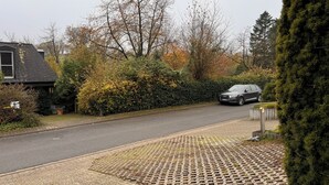 Uma rua residencial com calçada pavimentada, um carro estacionado e uma casa com porta de garagem visível.
