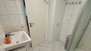 Uma casa de banho com uma sanita, chuveiro e um lava-pratos branco, e um tapete azul.