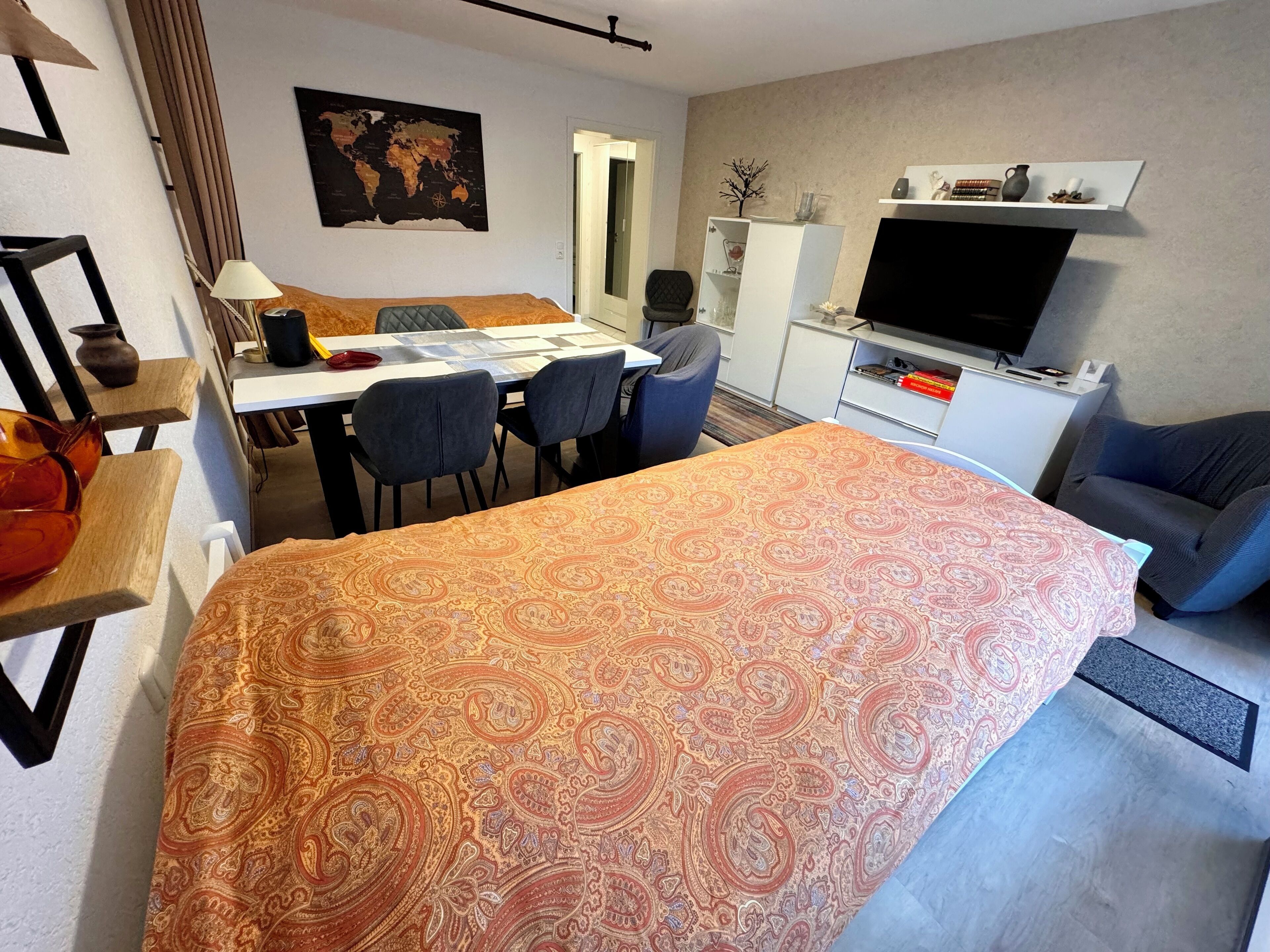 Ein Hotelzimmer mit einem großen Bett, einem Schreibtisch mit Stühlen, einem Fernseher und einer Weltkarte an der Wand.