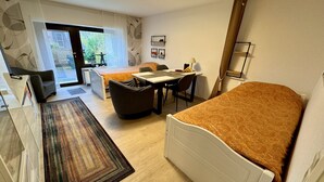 Quarto de hotel compacto com cama, escrivaninha e cadeira. Há uma pequena mesa com abajur e uma janela com vista para o exterior.
