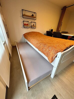 A compact room with a single bed, a desk, and a chair. There are wall-mounted shelves with decorative items. - Charming vacation apartment in Bergstein, Hürtgenwald  (Hürtgenwald)