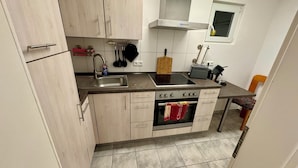 Cozinha compacta com pia, fogão e forno. Há armários e uma janela acima da pia.