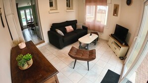 A living room with a sofa, coffee table, and TV stand. There is a dining area with a table and chairs.