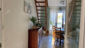 A hallway with a wooden staircase, a dining area with chairs and a table, and a potted plant on a cabinet.