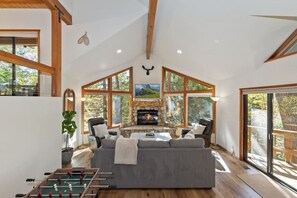 A spacious living room with a fireplace, large windows, and a cozy seating area. - Modern Treehouse w/ Spa | Stylish 3BR (Lake Arrowhead)