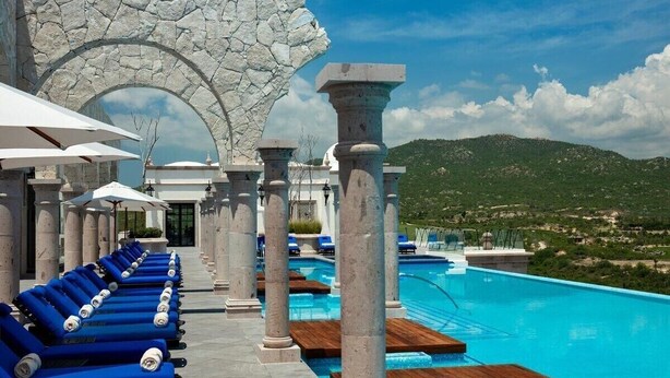 A poolside area with blue lounge chairs, stone columns, and a view of a mountainous landscape. - Charming ocean front 3-bdm  Cabo San Lucas, plunge pools  roof top pool and spa. (Cabo san Lucas)