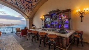 A bar area with a view of the sea, bar stools, and a decorative bar counter. - Charming ocean front 3-bdm  Cabo San Lucas, plunge pools  roof top pool and spa. (Cabo san Lucas)