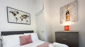 Un letto rifatto con cura, coperto da una tenda a lenzuolo rosa e bianca, con una testiera grigia e un quadro raffigurante una mappa del mondo sopra di esso.