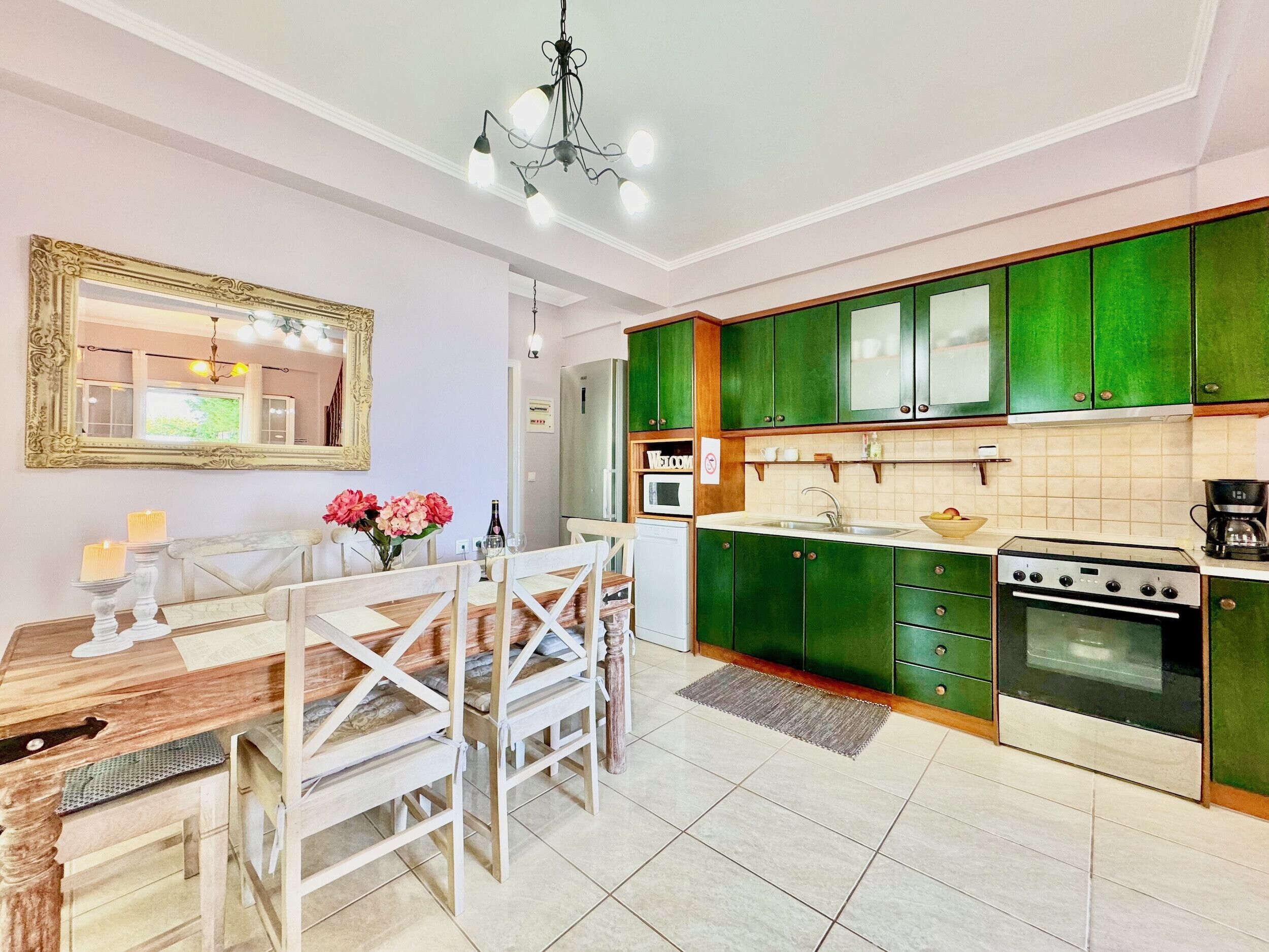Una cocina moderna con armarios verdes, una mesa de comedor con sillas y una araña.