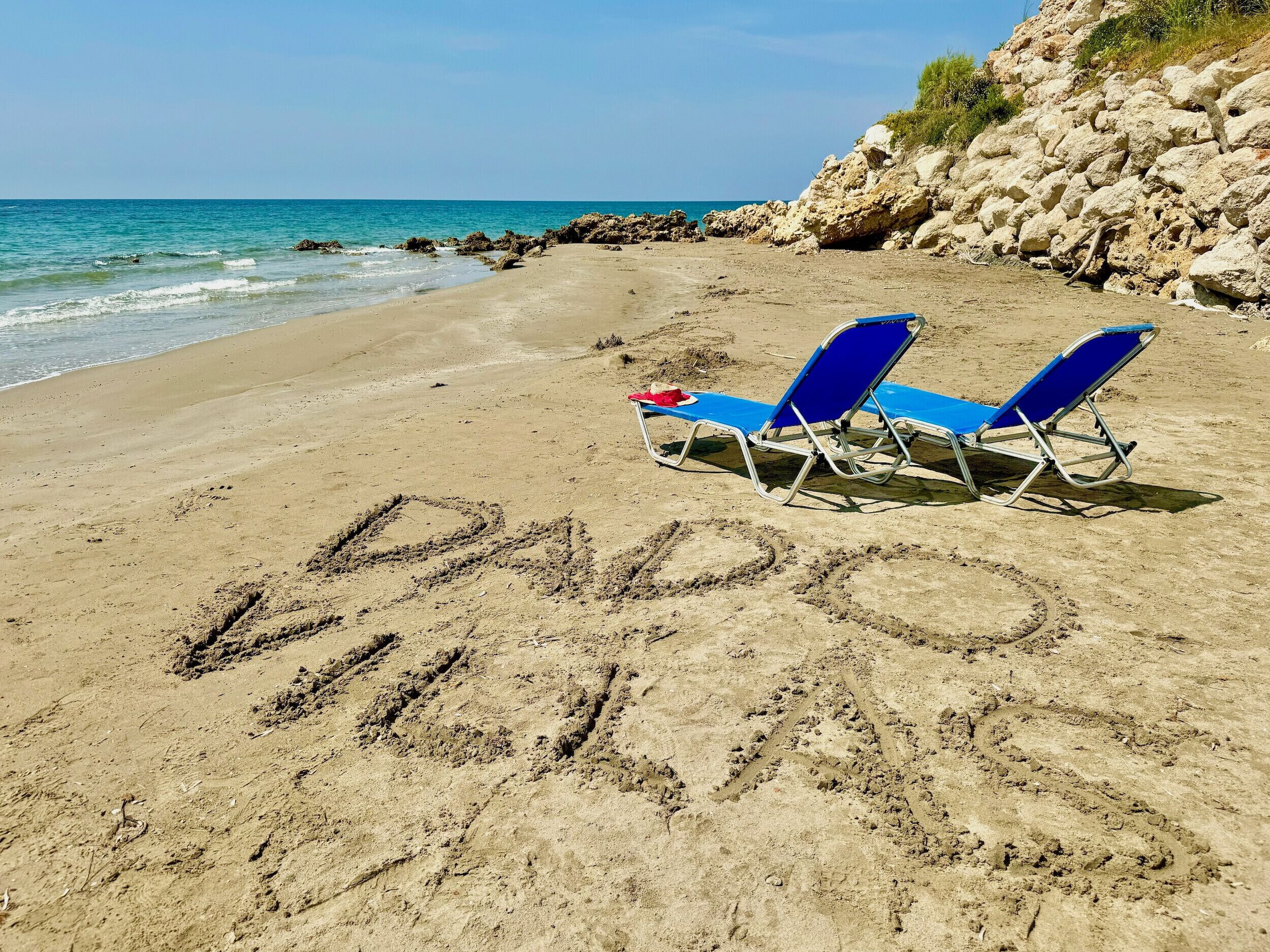 A beach with two blue lounge chairs and the word "PAPAS" written in the sand.