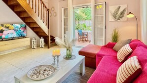 A living room with a wooden staircase, a TV, a coffee table with candles, a red sofa, and a view of the outdoors. - Beachfront Villa Rania with private pool (Chalikounas)
