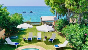 A poolside area with lounge chairs and umbrellas, overlooking a clear blue sea. - Beachfront Villa Rania with private pool (Chalikounas)