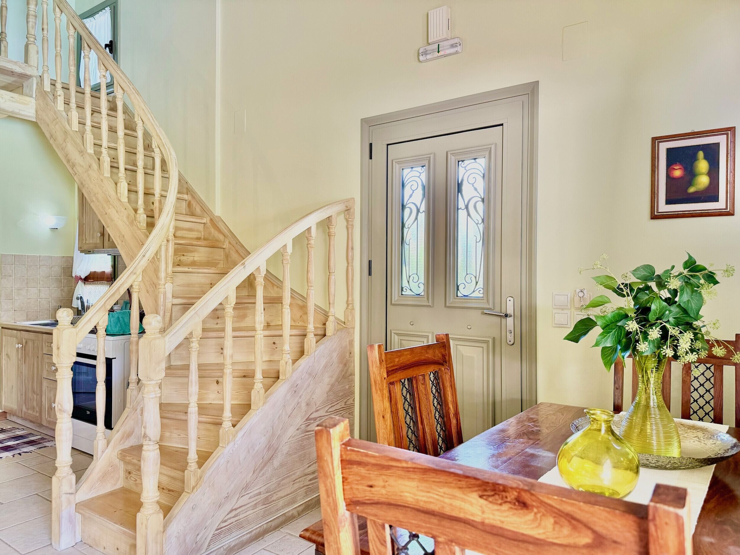 Una escalera de madera que lleva a un comedor con una mesa para dos personas, una silla y un jarrón con flores.